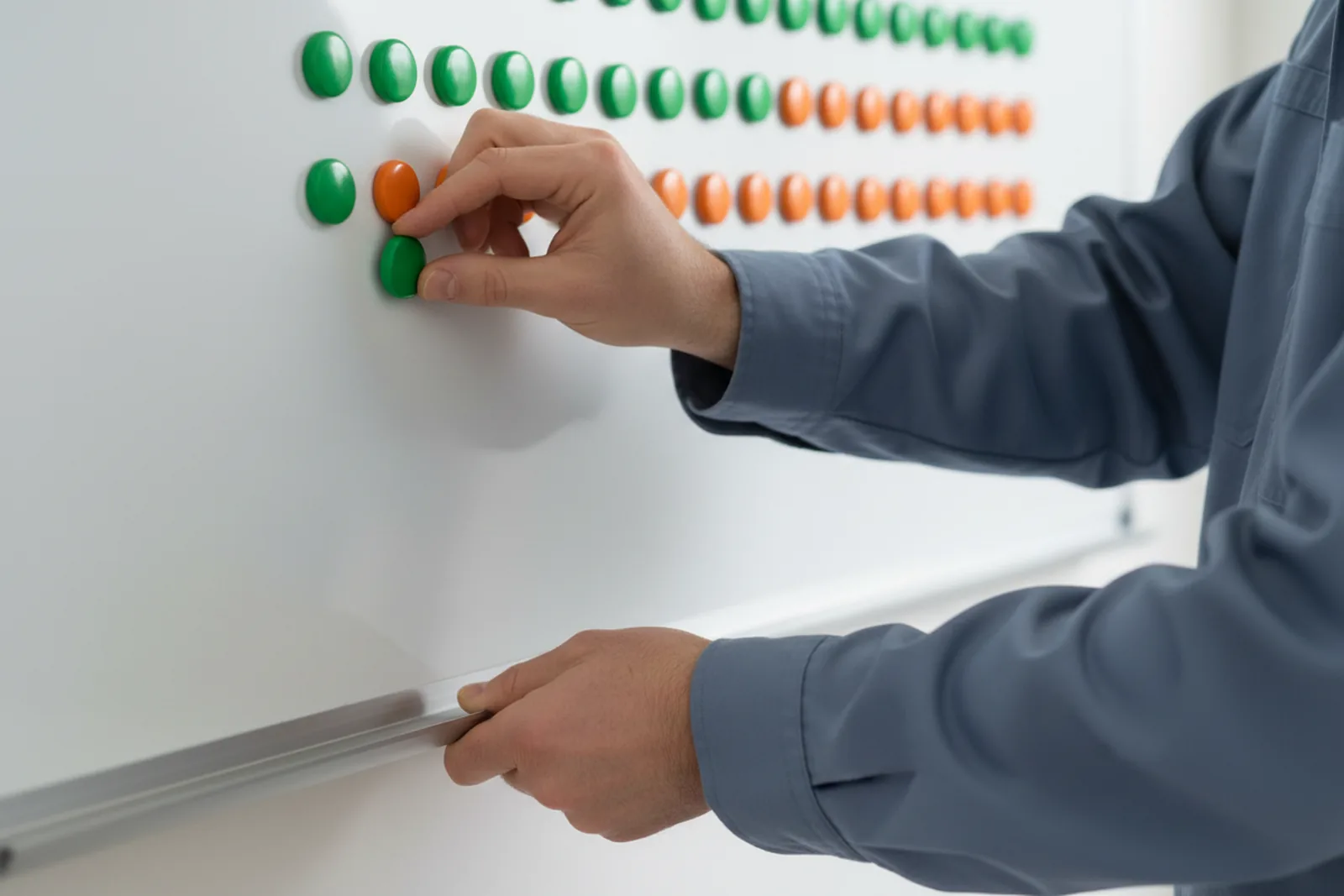 Close view of a person in a blue work shirt moving one green magnet on a white planner board.