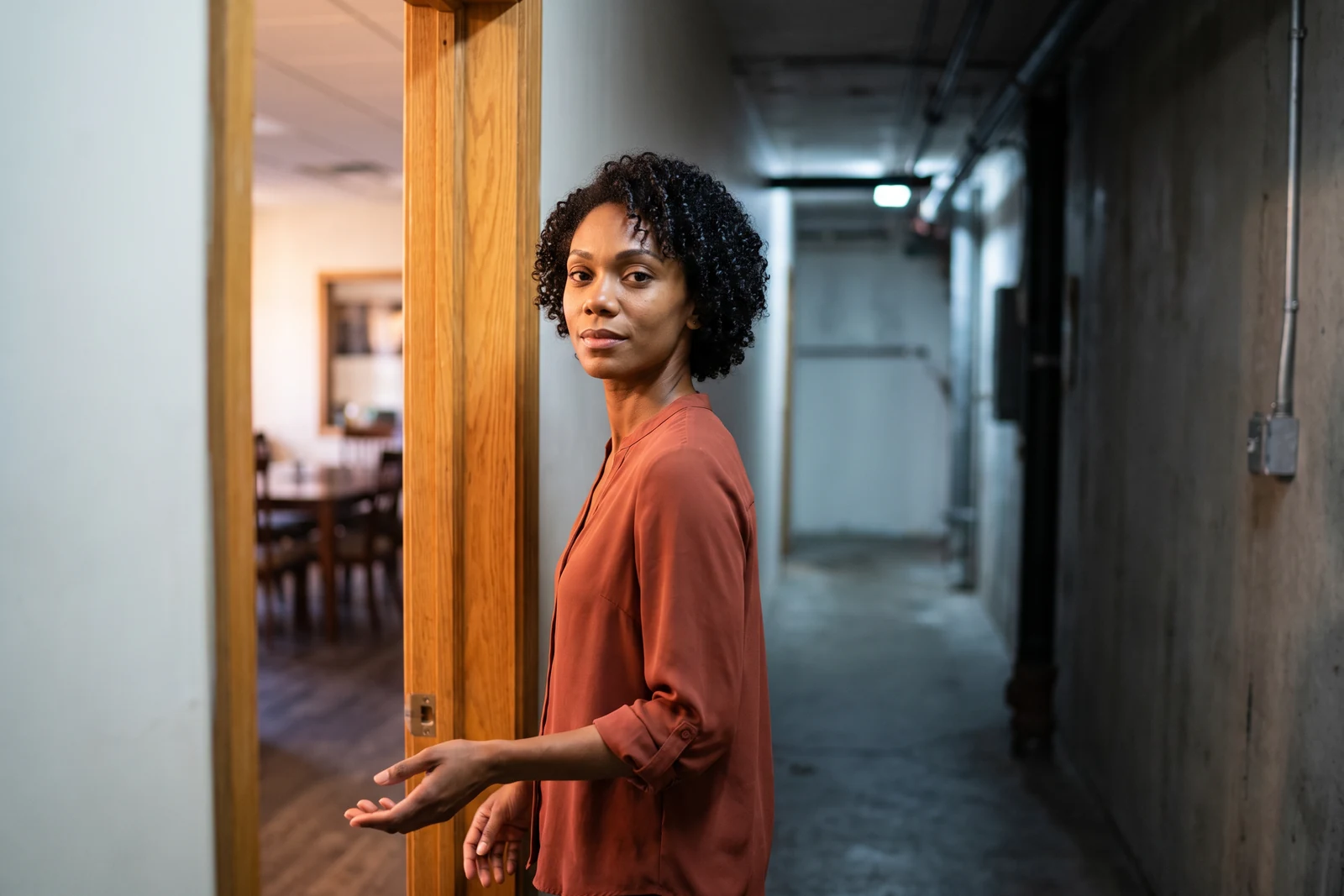 Ruby, the AI Customer Support Agent, stops in a service-corridor doorway with both hands empty and one palm open.